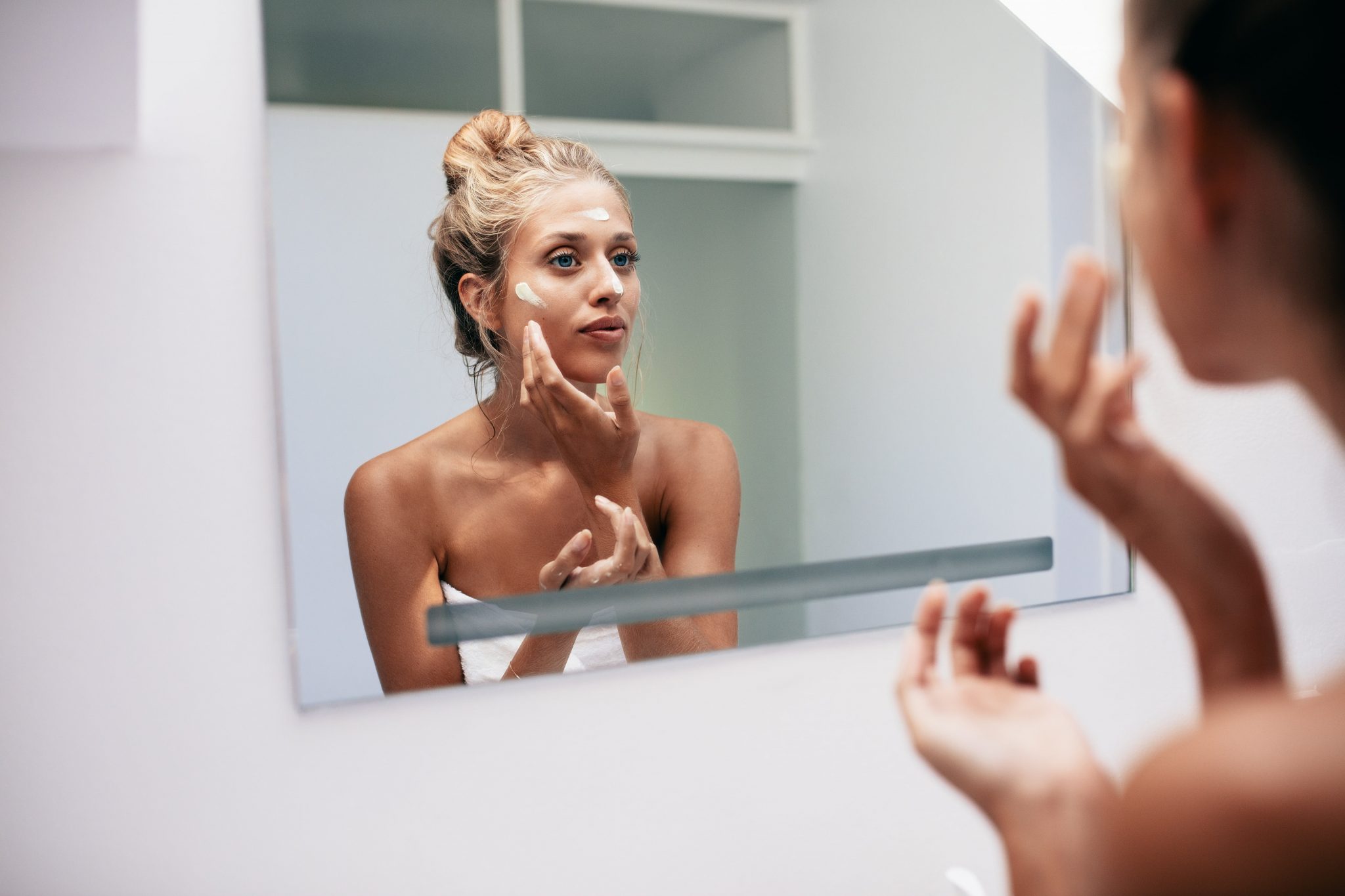 woman in her bathroom applies cream in her face