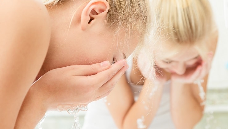 blonde hair woman washes her face with water
