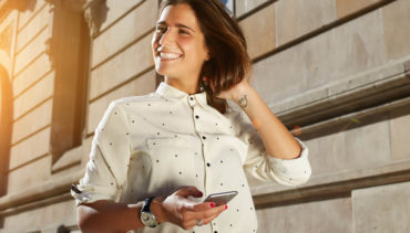 woman with white shirt holding her phone and smiling