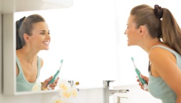 woman in front of her bathroom mirror brushes her teeth
