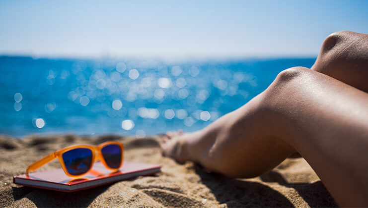 woman legs and orange sunglasses by the sea
