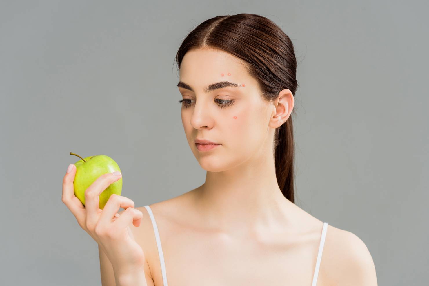 woman with acne looking at an apple she's holding