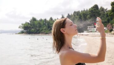 woman spraying sunscreen mist on the beach