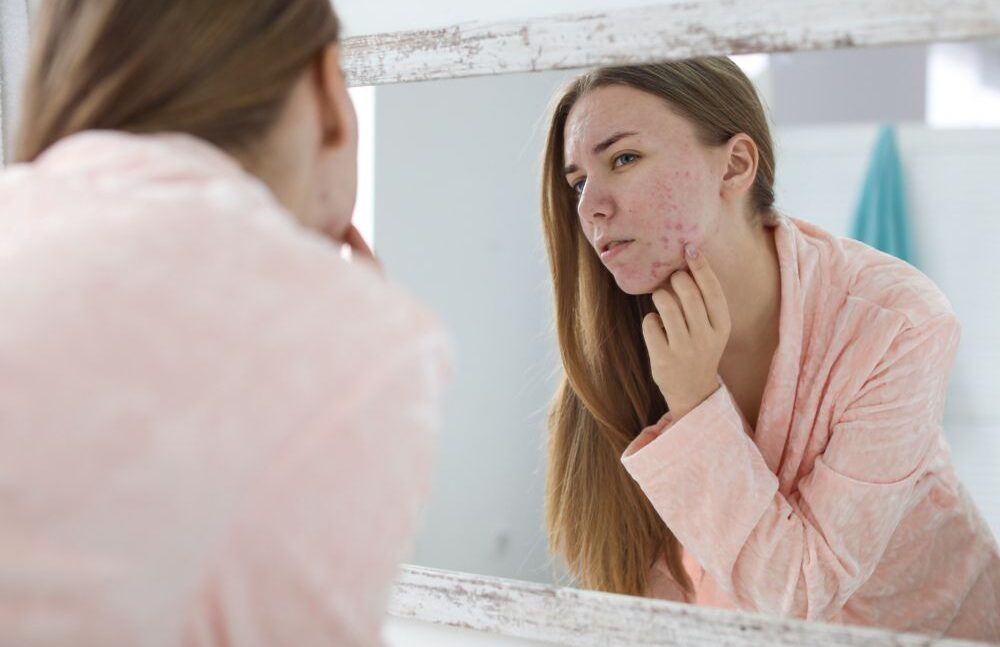 woman looking her face at the mirror