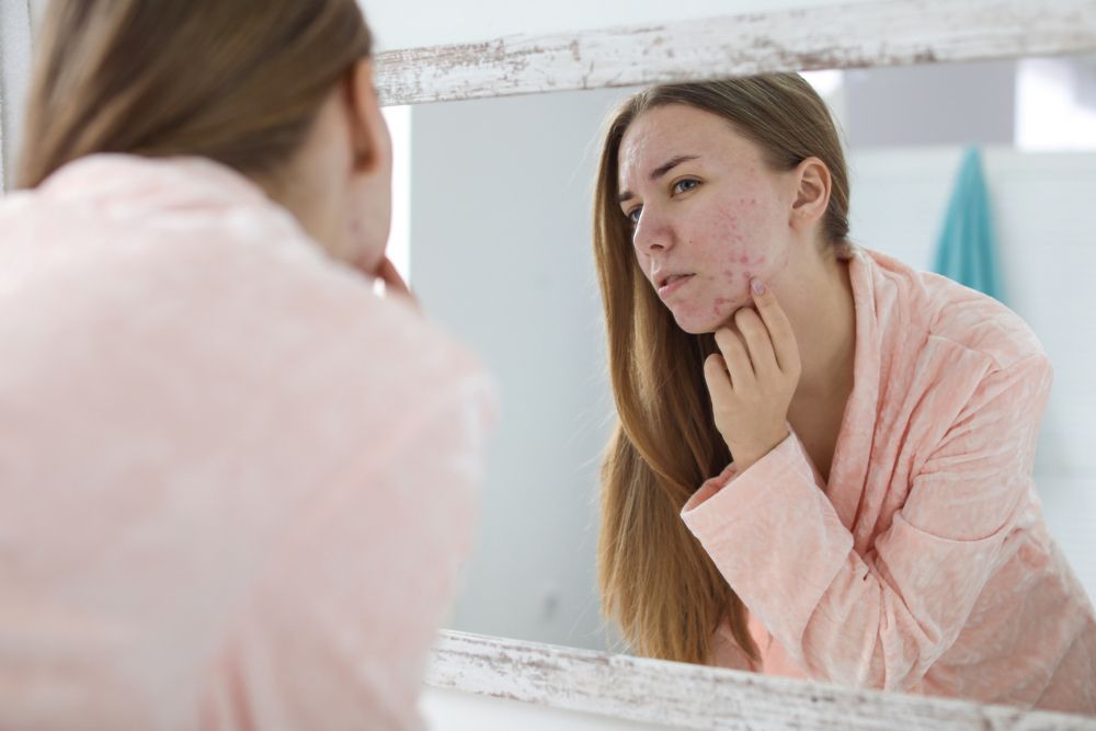woman looking her face at the mirror