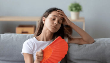 woman touching her hear with a hand fan